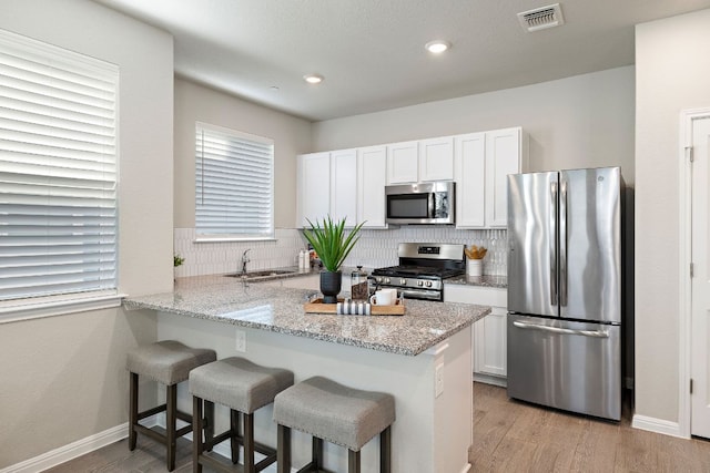 kitchen featuring a breakfast bar area, stainless steel appliances, backsplash, white cabinetry, and visible vents