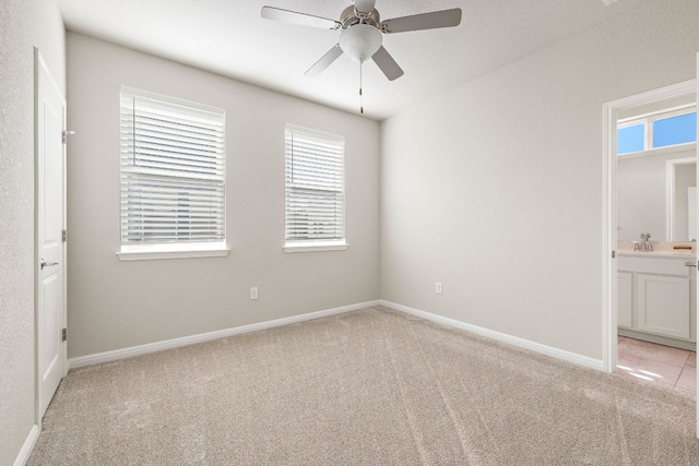 unfurnished bedroom with light colored carpet, connected bathroom, a ceiling fan, and baseboards