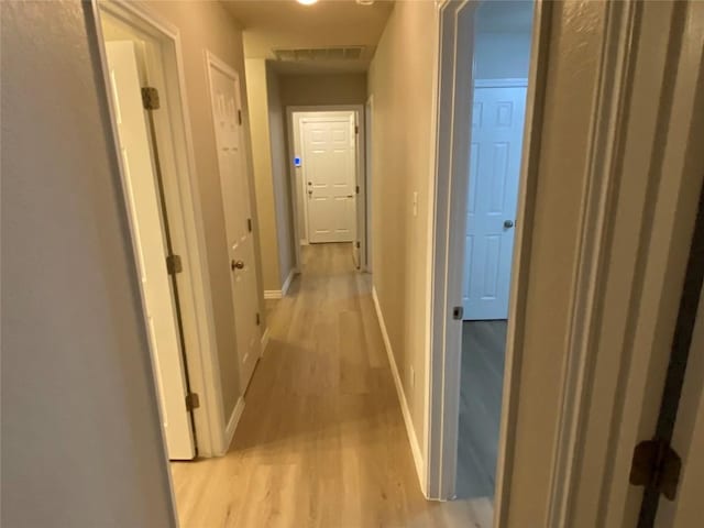 hallway featuring light wood finished floors, visible vents, and baseboards