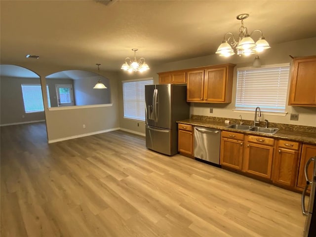 kitchen with a notable chandelier, a sink, appliances with stainless steel finishes, dark countertops, and brown cabinetry