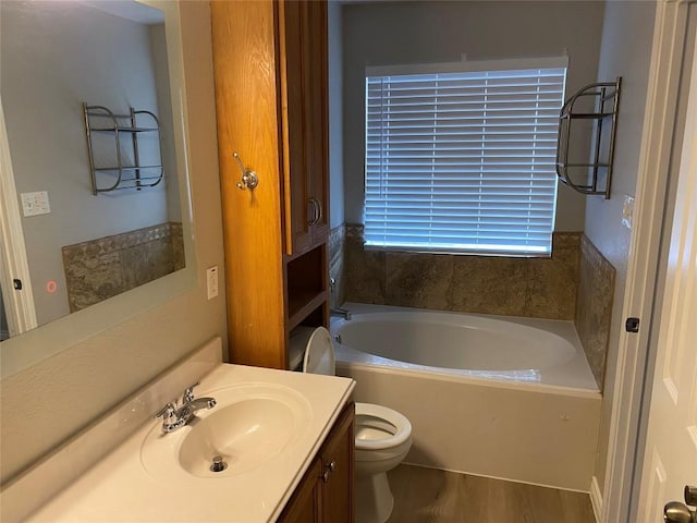bathroom with toilet, a bath, wood finished floors, and vanity