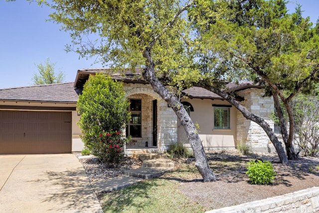 5200 Patagonia Pass, Austin, TX 78738 - view of property hidden behind natural elements featuring stone siding, a garage, driveway, stucco siding, and covered porch