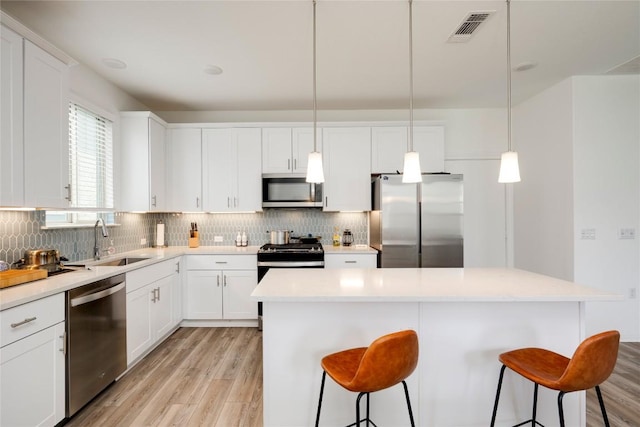 5408 Mars Ln, Austin, TX 78724 - kitchen with stainless steel appliances, a kitchen breakfast bar, light wood-type flooring, tasteful backsplash, and white cabinets