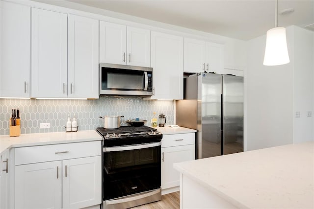 kitchen featuring white cabinetry, tasteful backsplash, appliances with stainless steel finishes, light wood-type flooring, and hanging light fixtures