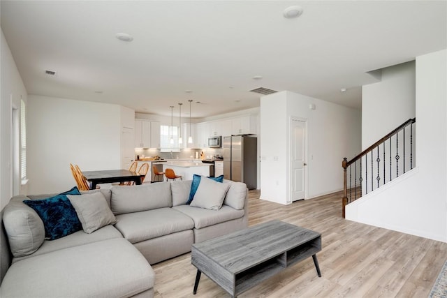 living room with stairway, visible vents, light wood-style flooring, and baseboards