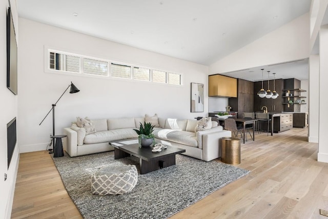 living room featuring light wood-type flooring, vaulted ceiling, and baseboards