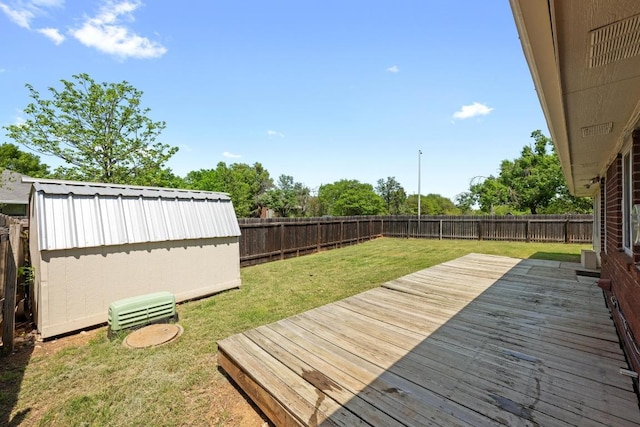 deck with a storage unit, a fenced backyard, a lawn, and an outbuilding
