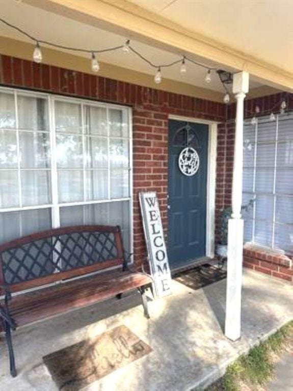 doorway to property with covered porch and brick siding