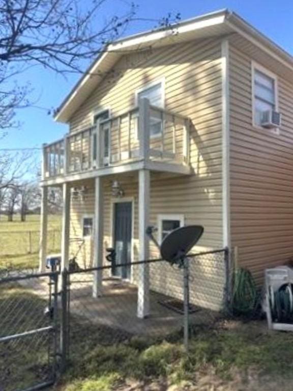 view of property exterior with a balcony, cooling unit, fence, and a gate