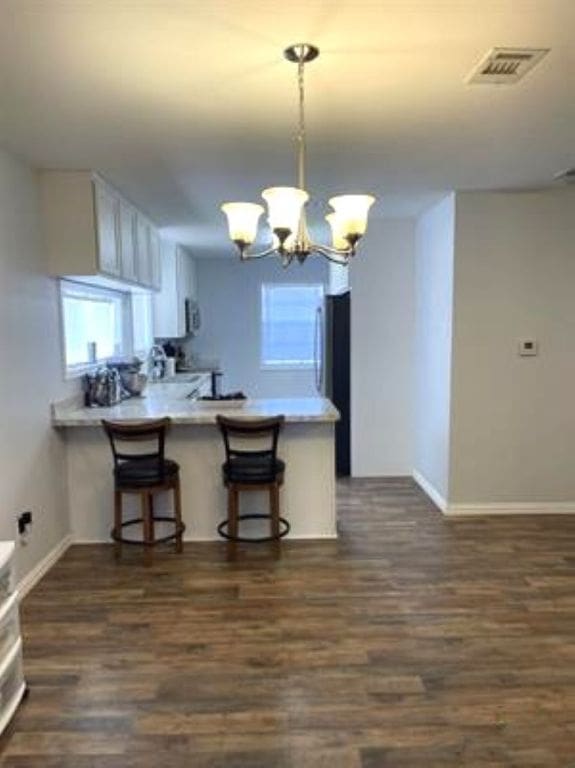 kitchen with a peninsula, a notable chandelier, dark wood finished floors, and visible vents