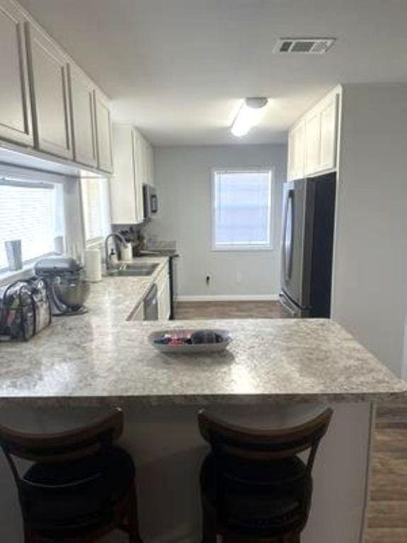 kitchen featuring visible vents, a sink, freestanding refrigerator, a breakfast bar, and a peninsula