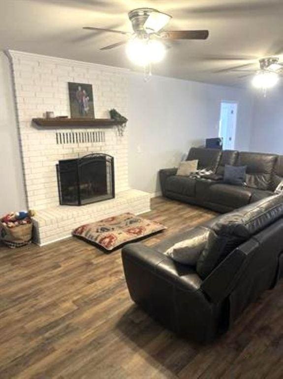 living area with wood finished floors, ceiling fan, and a brick fireplace