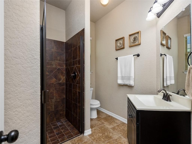 bathroom with a shower stall, vanity, toilet, a textured wall, and baseboards