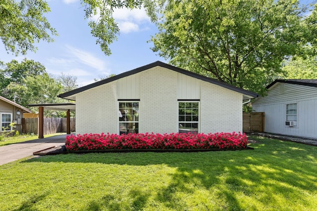 view of side of home featuring fence, brick siding, concrete driveway, a lawn, and a carport