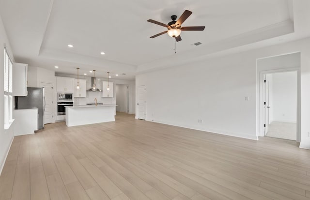 329 Singing Dove Way, Liberty Hill, TX 78642 - unfurnished living room featuring a tray ceiling, ceiling fan, light wood-type flooring, and recessed lighting