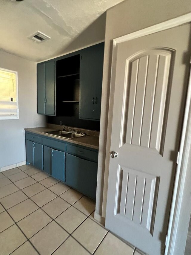 kitchen featuring light tile patterned floors, open shelves, dark countertops, visible vents, and a sink