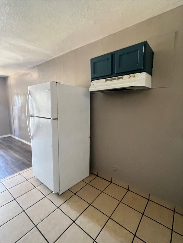 kitchen featuring freestanding refrigerator, light tile patterned floors, a textured ceiling, under cabinet range hood, and light countertops