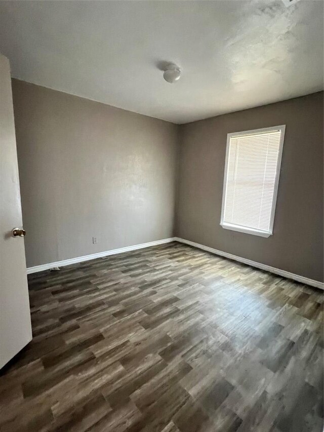 spare room with dark wood-type flooring and baseboards