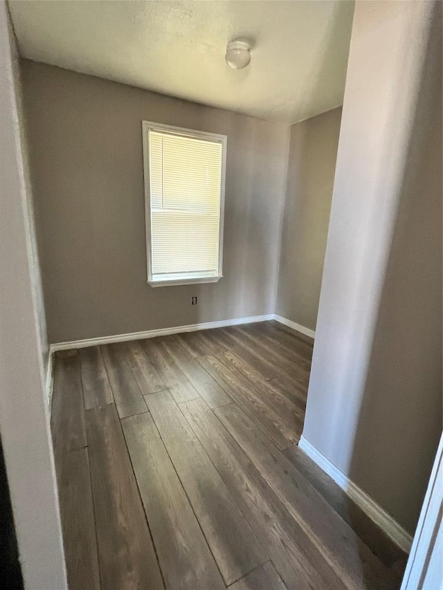 unfurnished room with dark wood-type flooring and baseboards