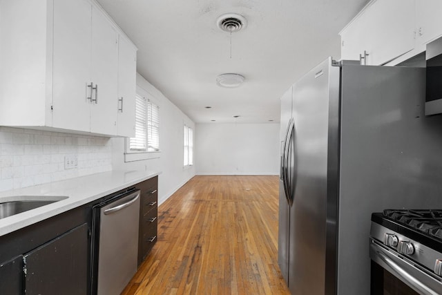 207 W 39th St, Austin, TX 78751 - kitchen featuring stainless steel appliances, light countertops, white cabinets, decorative backsplash, and light wood-style flooring