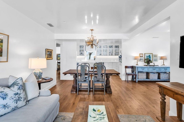 living area with an inviting chandelier, baseboards, wood finished floors, and visible vents