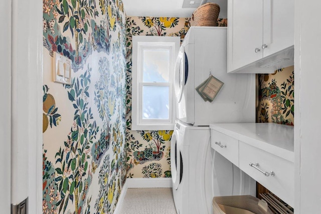 clothes washing area featuring cabinet space, stacked washer and dryer, wallpapered walls, and baseboards