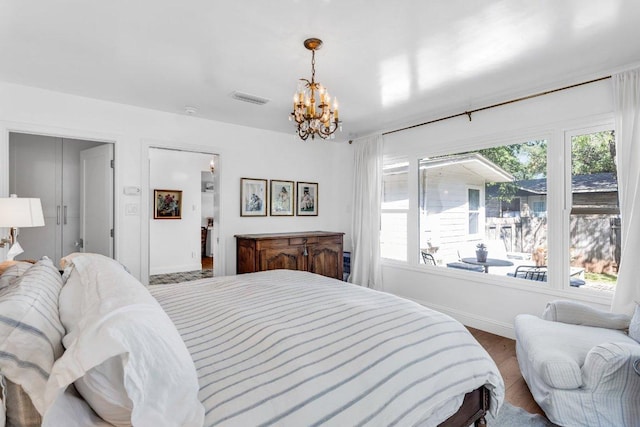 bedroom with visible vents, baseboards, wood finished floors, and a notable chandelier