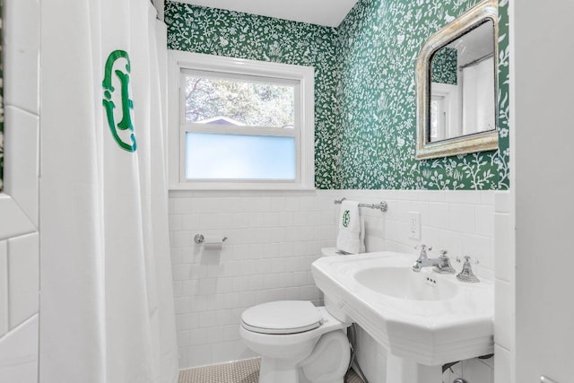 bathroom featuring a sink, toilet, a wainscoted wall, wallpapered walls, and tile walls