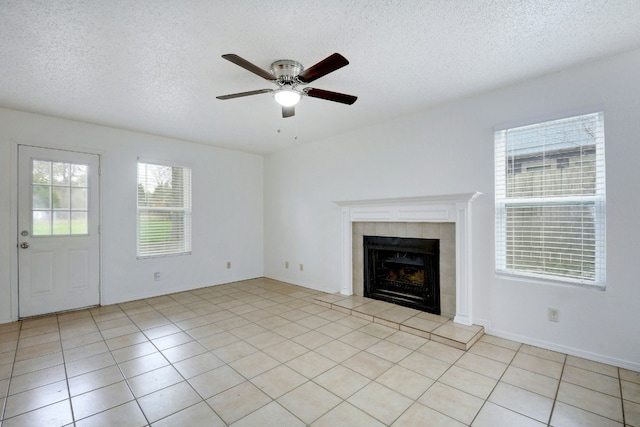 unfurnished living room featuring a textured ceiling, ceiling fan, a tiled fireplace, and light tile patterned floors