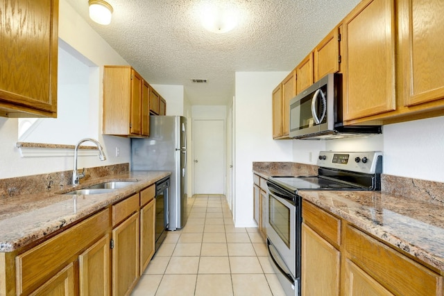 kitchen featuring light tile patterned floors, a sink, a textured ceiling, light stone countertops, and stainless steel appliances