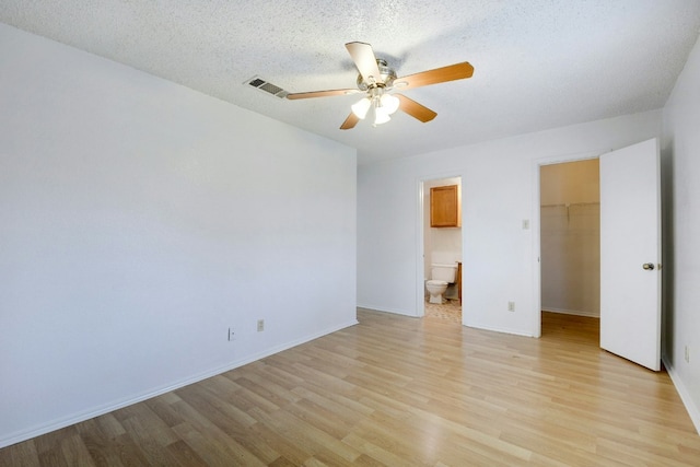 unfurnished bedroom featuring baseboards, a closet, a walk in closet, light wood-style floors, and visible vents