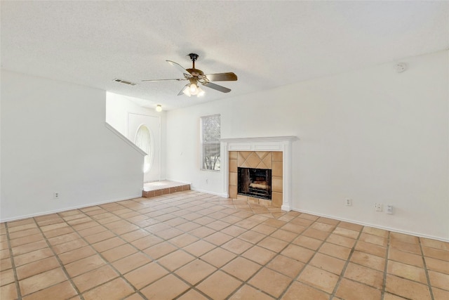 unfurnished living room featuring a tiled fireplace, light tile patterned floors, a textured ceiling, visible vents, and ceiling fan