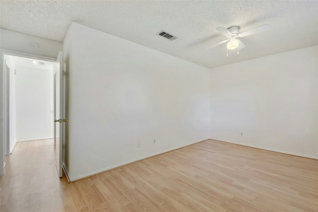 spare room with baseboards, light wood-type flooring, a textured ceiling, a ceiling fan, and visible vents