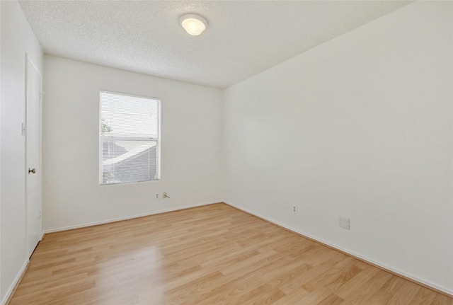 spare room featuring light wood-style floors, baseboards, and a textured ceiling