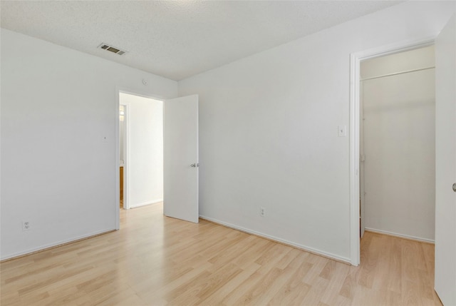 unfurnished bedroom featuring visible vents, baseboards, a closet, a walk in closet, and wood finished floors