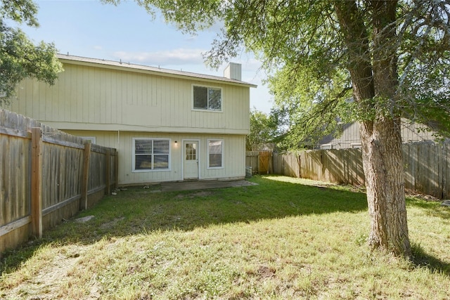 back of property with a fenced backyard, a chimney, and a lawn