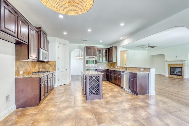 2801 Mirasol Dr, Round Rock, TX 78681 - kitchen featuring arched walkways, appliances with stainless steel finishes, a peninsula, ceiling fan, and tasteful backsplash