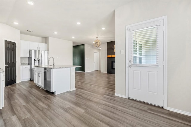 kitchen featuring a notable chandelier, white cabinets, a kitchen island with sink, stainless steel appliances, and wood finished floors