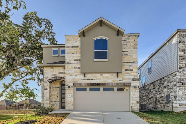 view of front of house with stucco siding, driveway, stone siding, an attached garage, and central AC unit