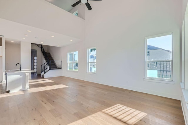 unfurnished living room with light wood-style floors, baseboards, a ceiling fan, and stairs