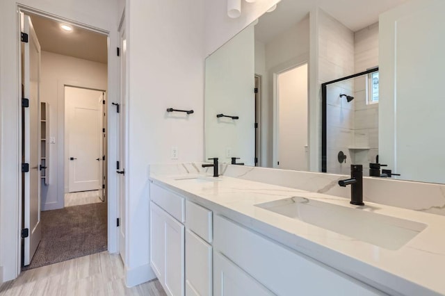 full bath featuring a shower stall, double vanity, a sink, and wood finished floors