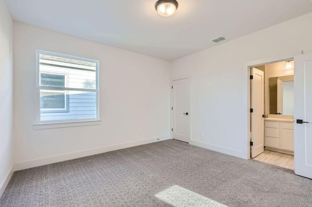 unfurnished bedroom featuring visible vents, baseboards, connected bathroom, and light carpet