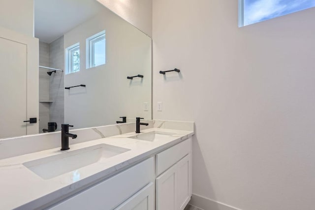 bathroom featuring a sink, walk in shower, double vanity, and baseboards