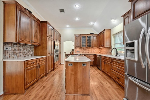kitchen with stainless steel appliances, crown molding, a kitchen island, a sink, and light wood finished floors