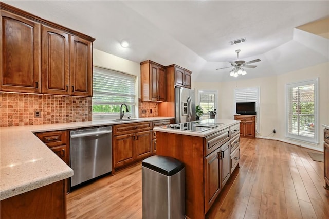 kitchen with appliances with stainless steel finishes, a sink, backsplash, light wood-type flooring, and lofted ceiling