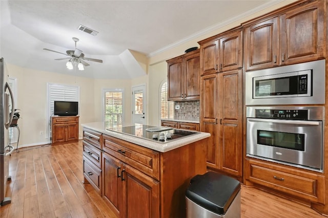 kitchen with appliances with stainless steel finishes, ceiling fan, light wood-type flooring, a center island, and tasteful backsplash