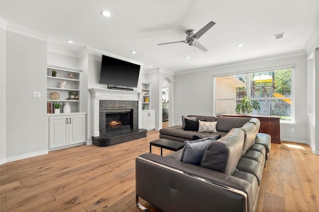living room with crown molding, light wood-type flooring, a ceiling fan, recessed lighting, and a fireplace