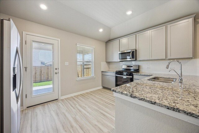 kitchen with appliances with stainless steel finishes, a sink, decorative backsplash, light wood-type flooring, and lofted ceiling