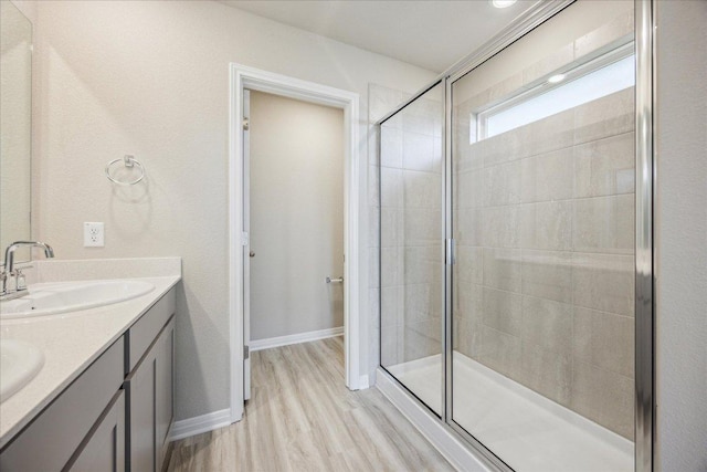bathroom featuring a stall shower, wood finished floors, double vanity, and baseboards