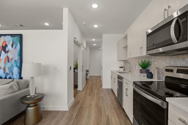 6324 N Lamar Blvd Unit 313, Austin, TX 78752 - kitchen featuring appliances with stainless steel finishes, a sink, a barn door, light countertops, and tasteful backsplash